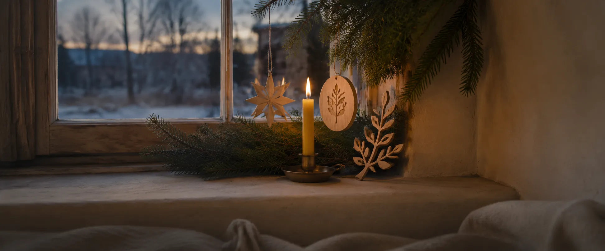 Fensterbank mit brennender Kerze und Weihnachtsdeko aus Holz vor verschneiter Landschaft