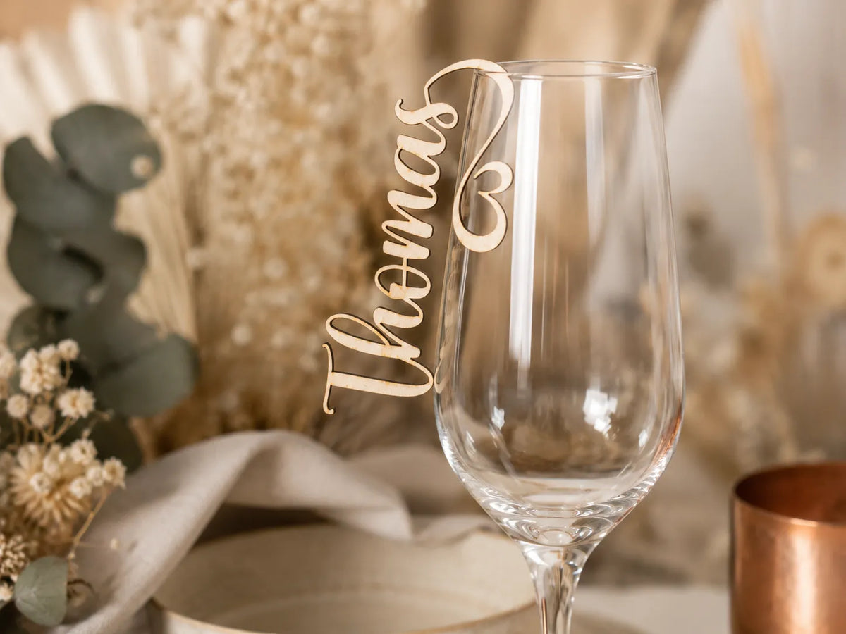 Sektglas mit graviertem Namensanhänger aus Holz auf einer Hochzeitstafel mit Trockenblumen