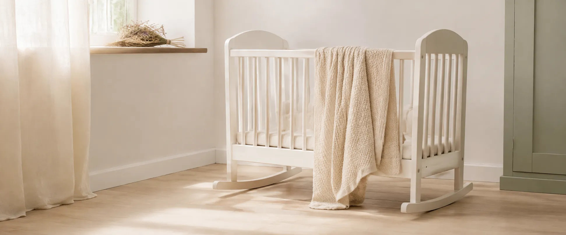 Weißes Babybett mit heller Decke am sonnigen Fenster eines ruhigen Kinderzimmers
