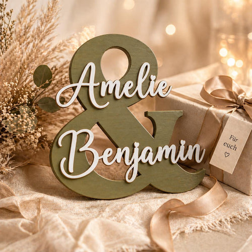 Personalisiertes &-Namensschild aus olivgrünem Birkensperrholz mit den Namen Amelie und Benjamin, dekoriert mit Trockenblumen und Geschenkbox