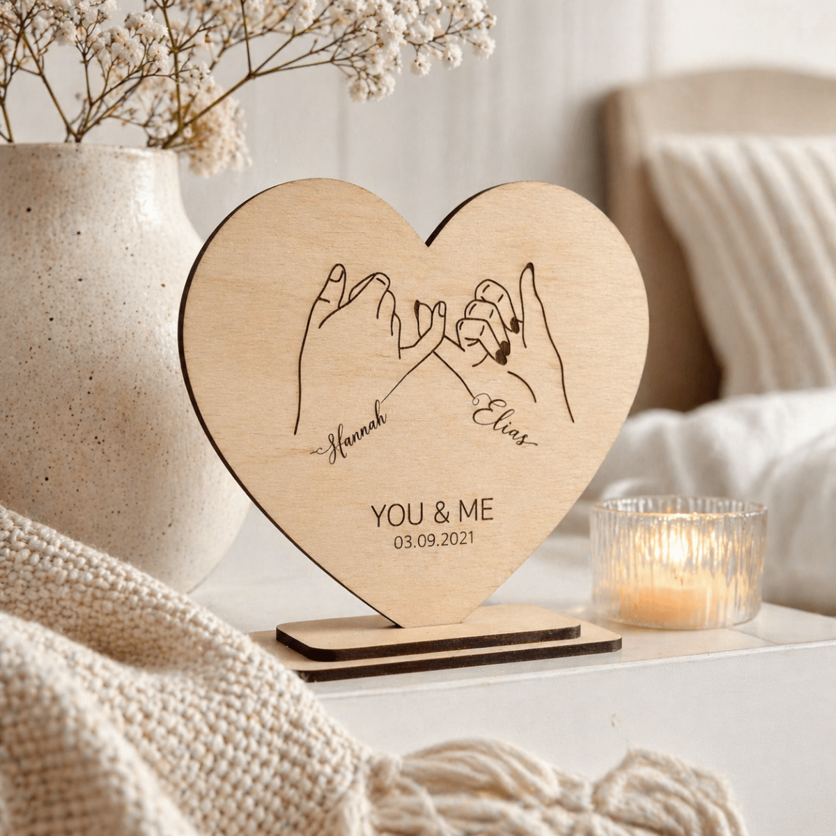 Holzherz auf Standfuß neben Vase und Kerze im Wohnzimmer