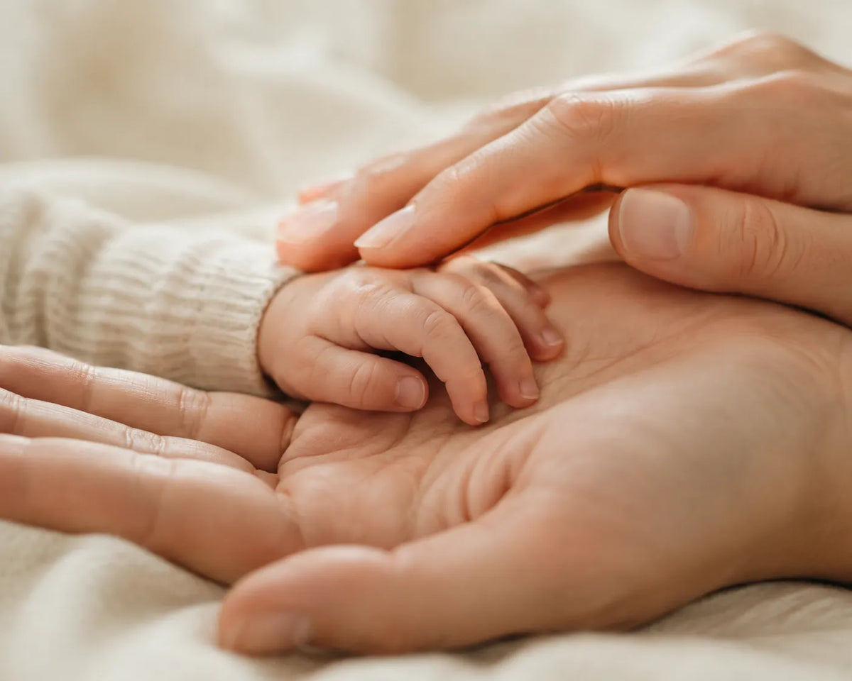 Winzige Babyhand liegt in den geöffneten Händen der Eltern auf einer weichen Decke